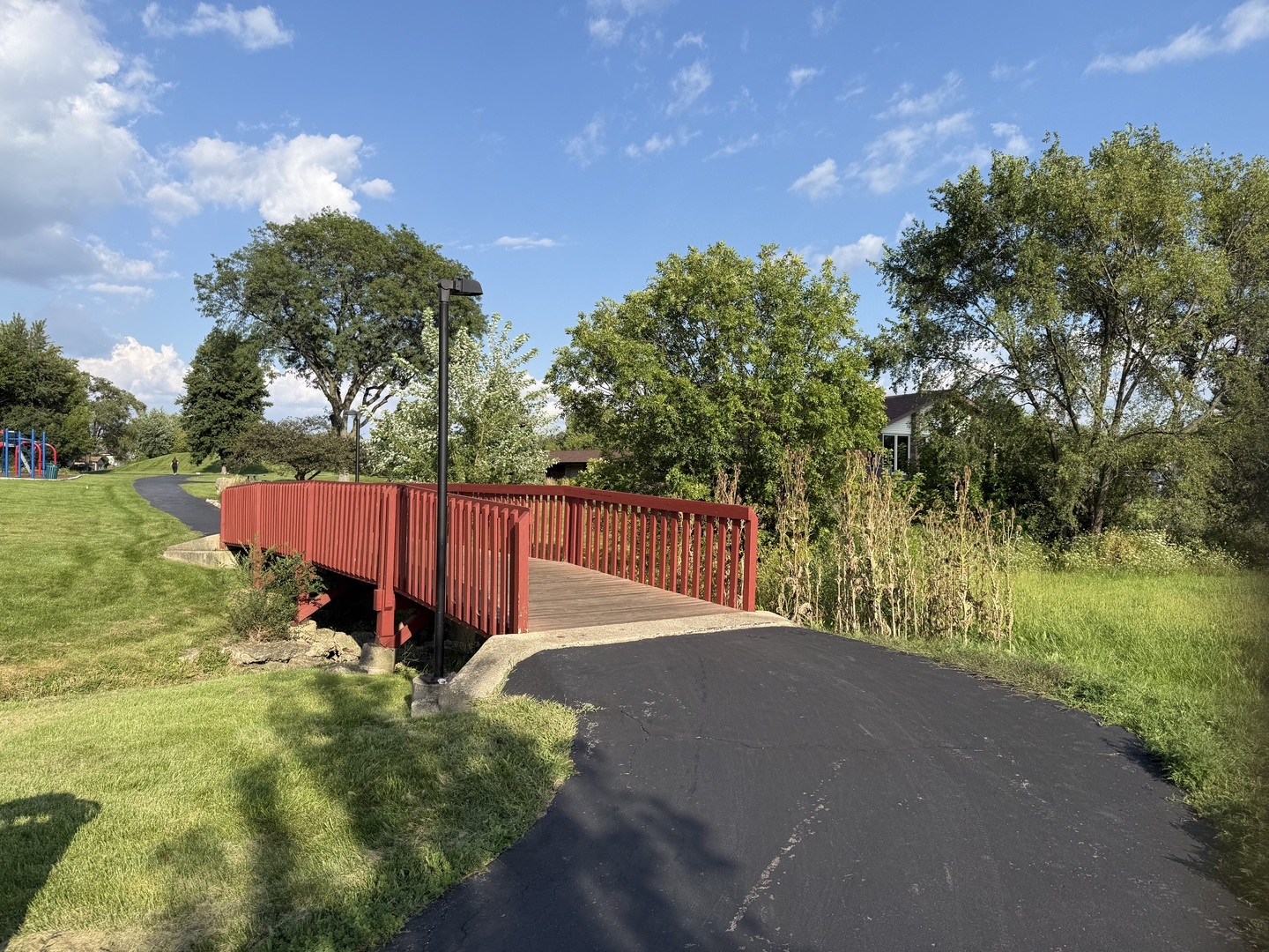 Neighborhood park with a red pedestrian bridge, paved path, and playground.