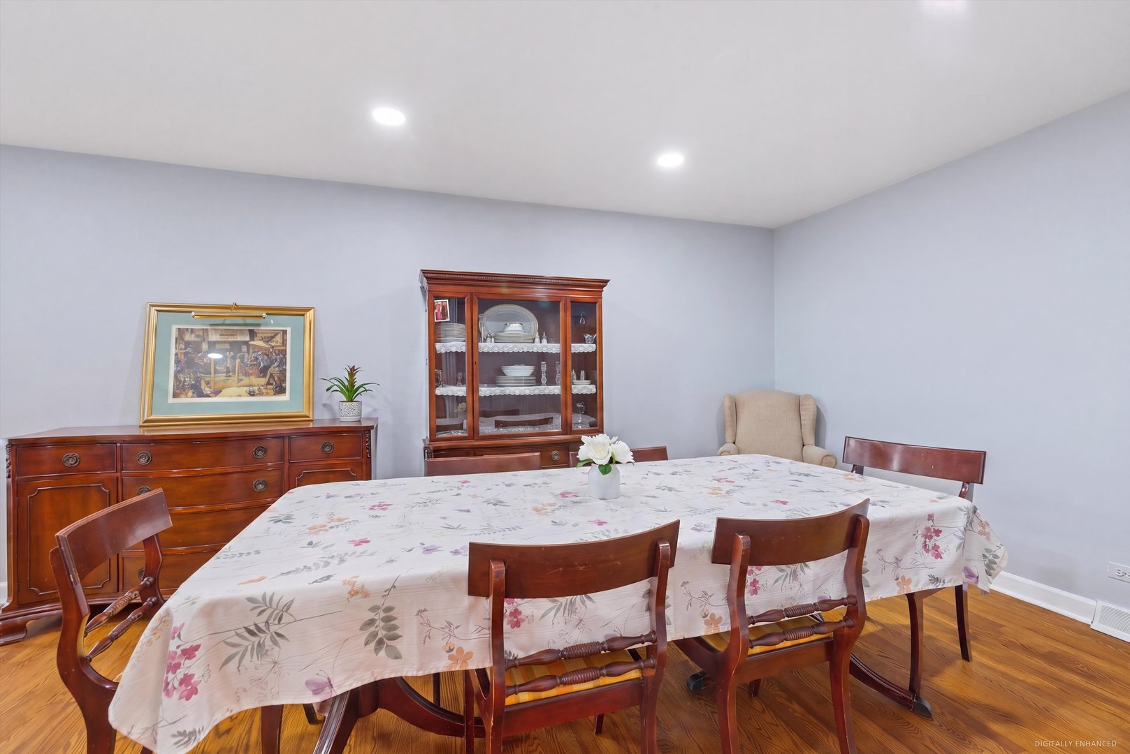 Dining room with a floral tablecloth, dark wood furniture, and glass-front china cabinet.