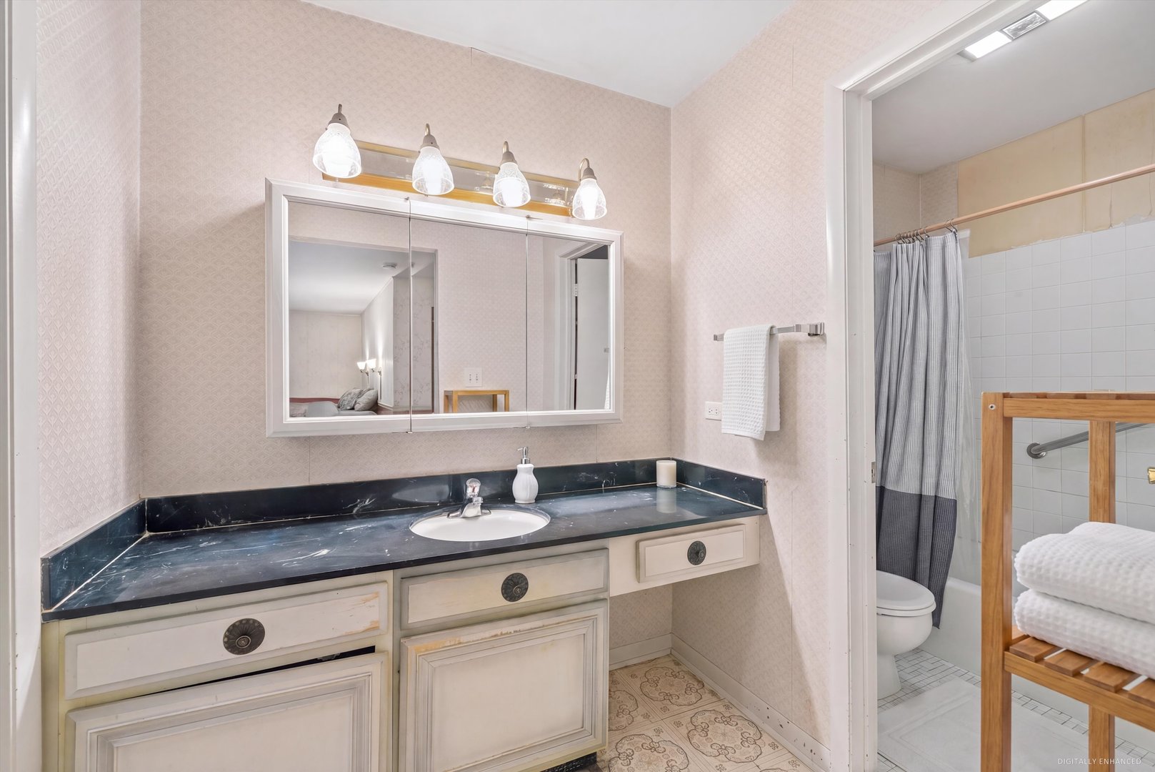 Bathroom vanity with dark countertop and mirrored cabinet; doorway opens to a tiled shower and toilet.