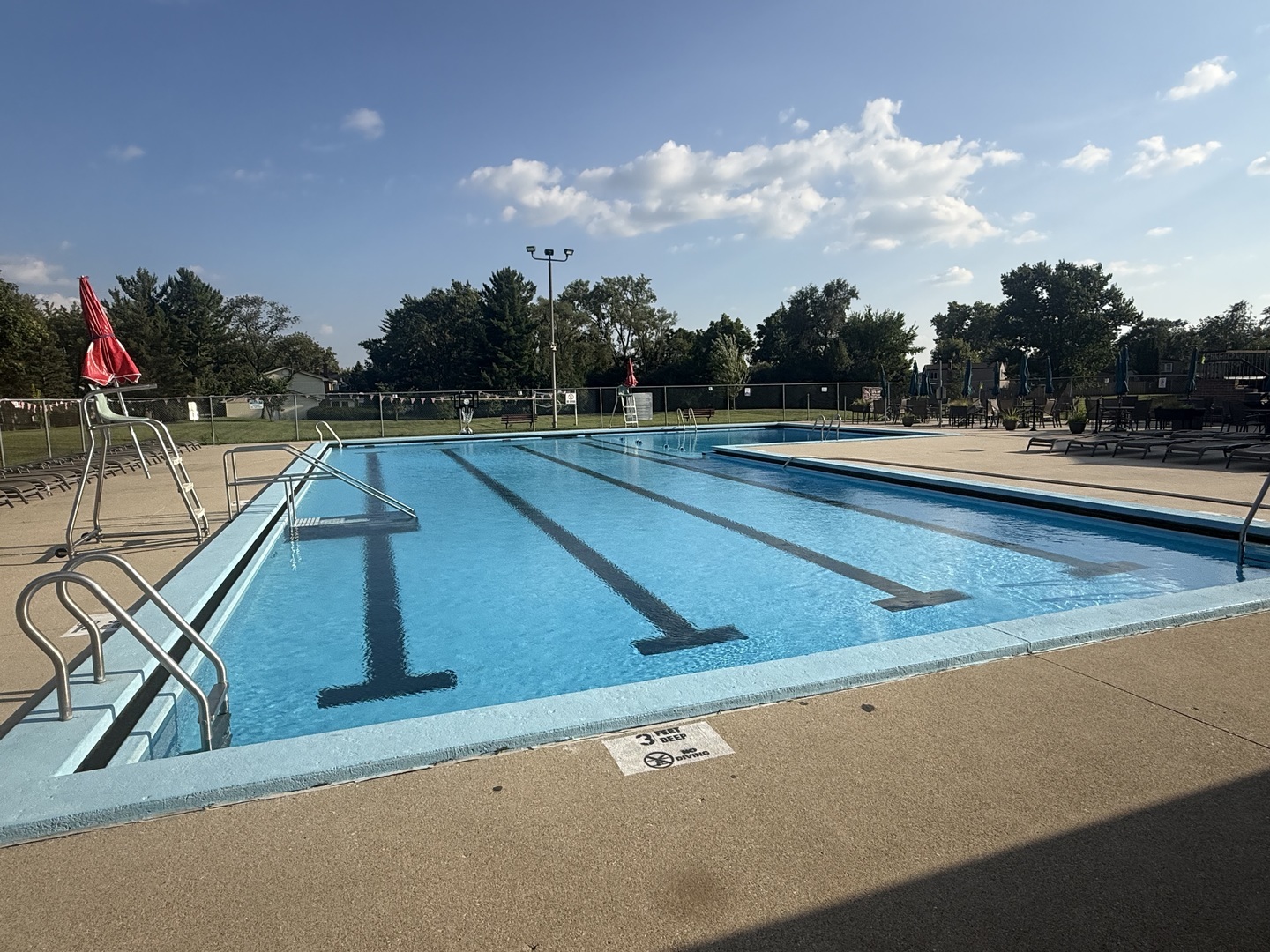 Outdoor pool with dark lap lanes, metal ladders, and a broad concrete deck.