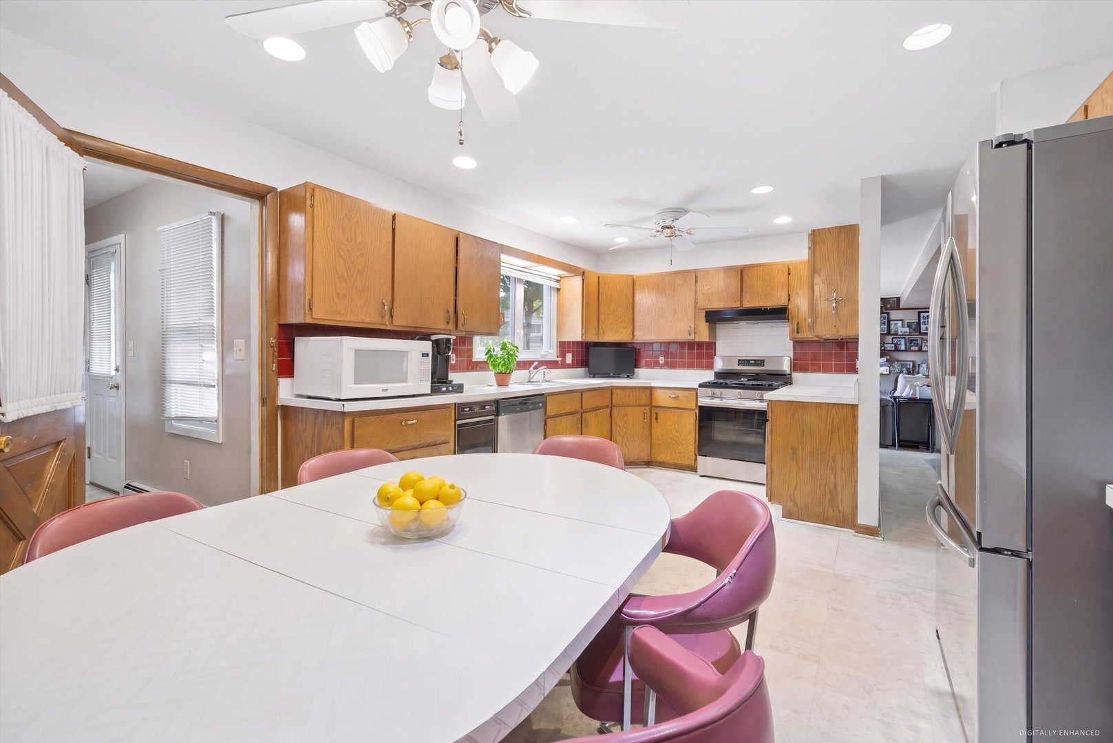 Kitchen with wood cabinets, red tile backsplash, stainless appliances, and a large dining table with pink chairs.