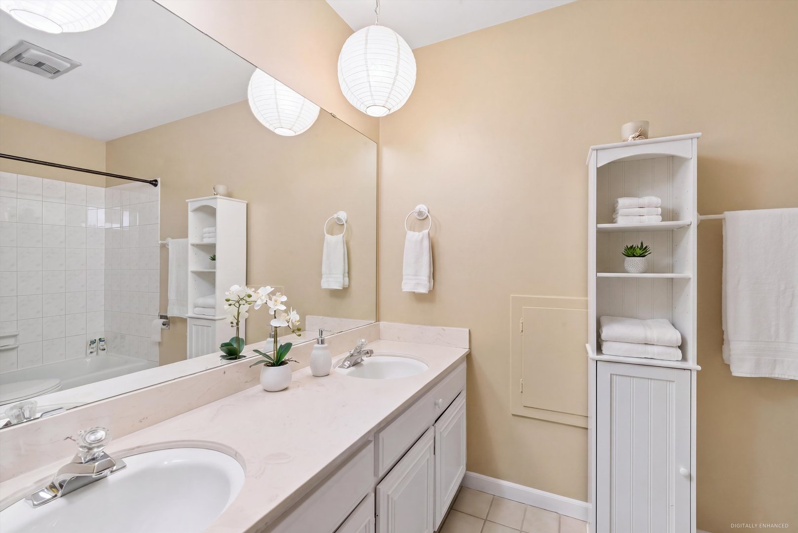 Bathroom with double-sink vanity, tiled tub and shower, and white linen cabinet.
