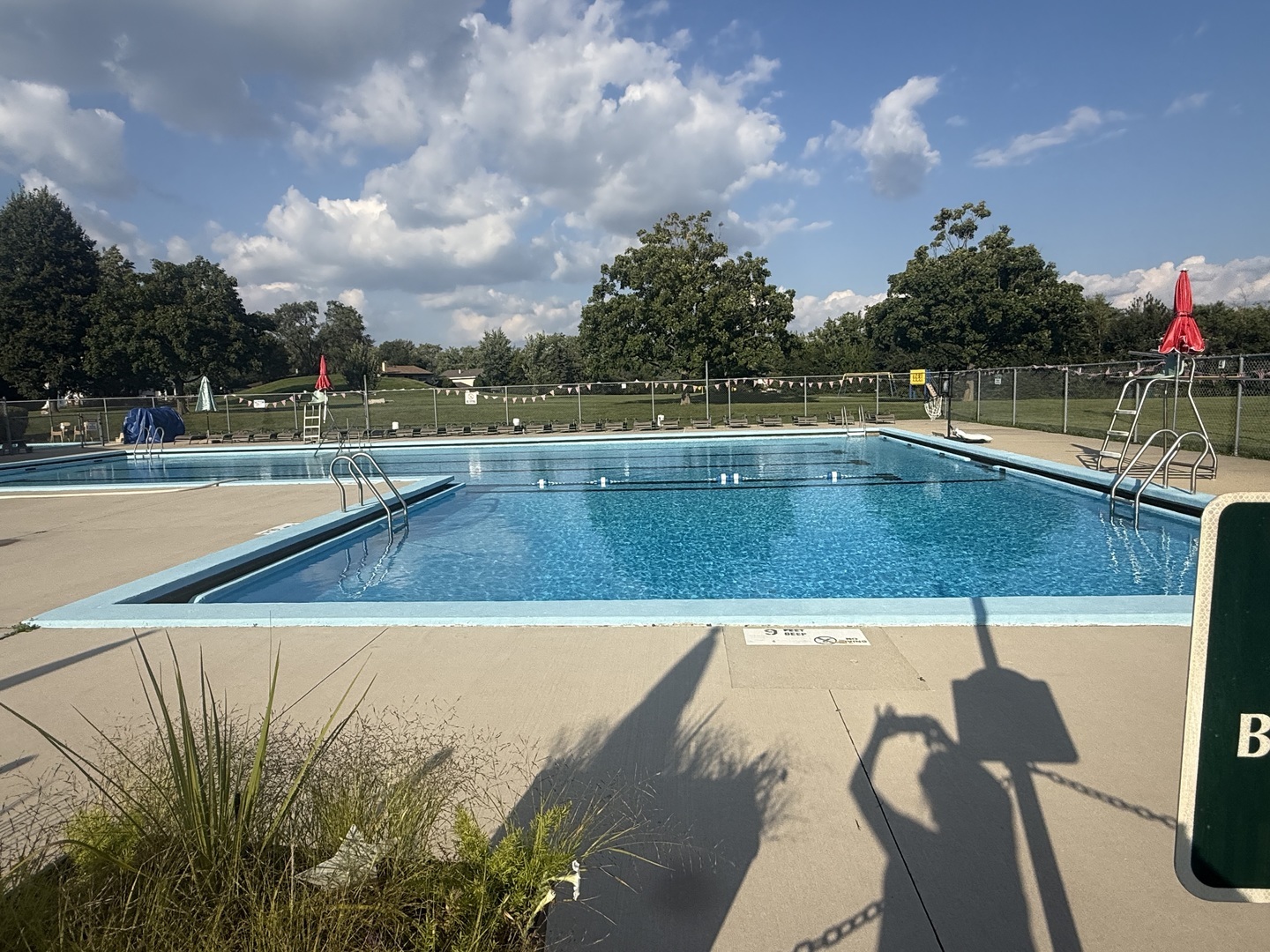 Outdoor community pool with turquoise water, metal ladders, and a fenced lawn.