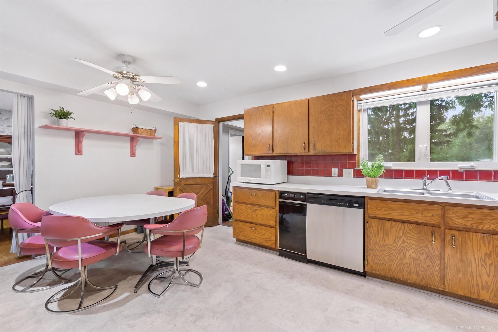 Kitchen and dining area with oak cabinets, red tile backsplash, and a white table with pink chairs.