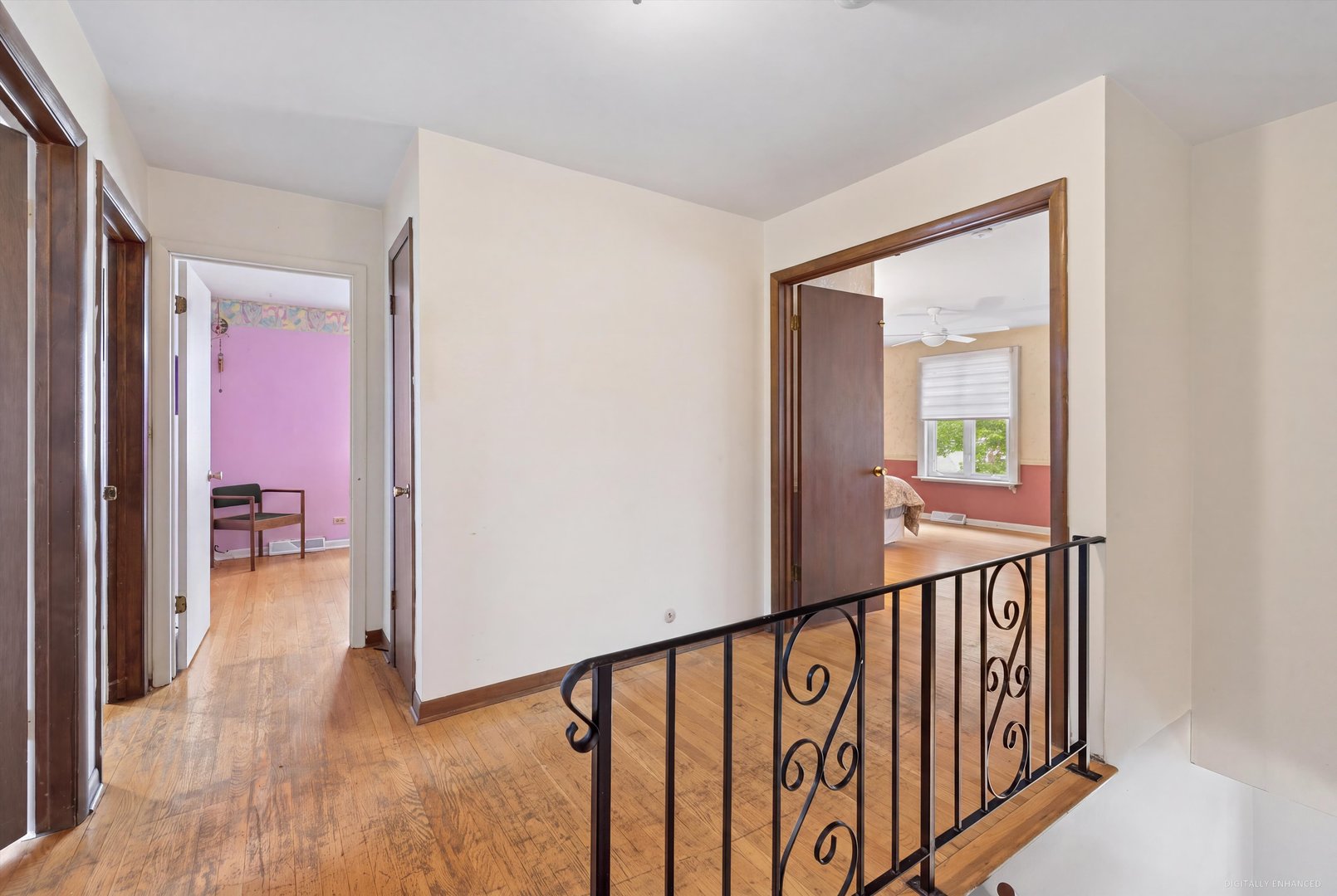 Upstairs landing with hardwood floors and wrought-iron railing, overlooking open doorways to two bedrooms.