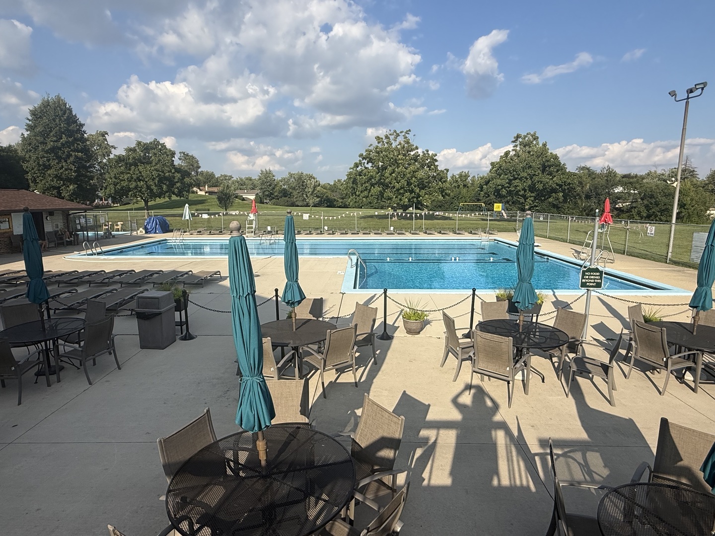 Community pool deck with two swimming pools, outdoor tables, chairs, and teal umbrellas.