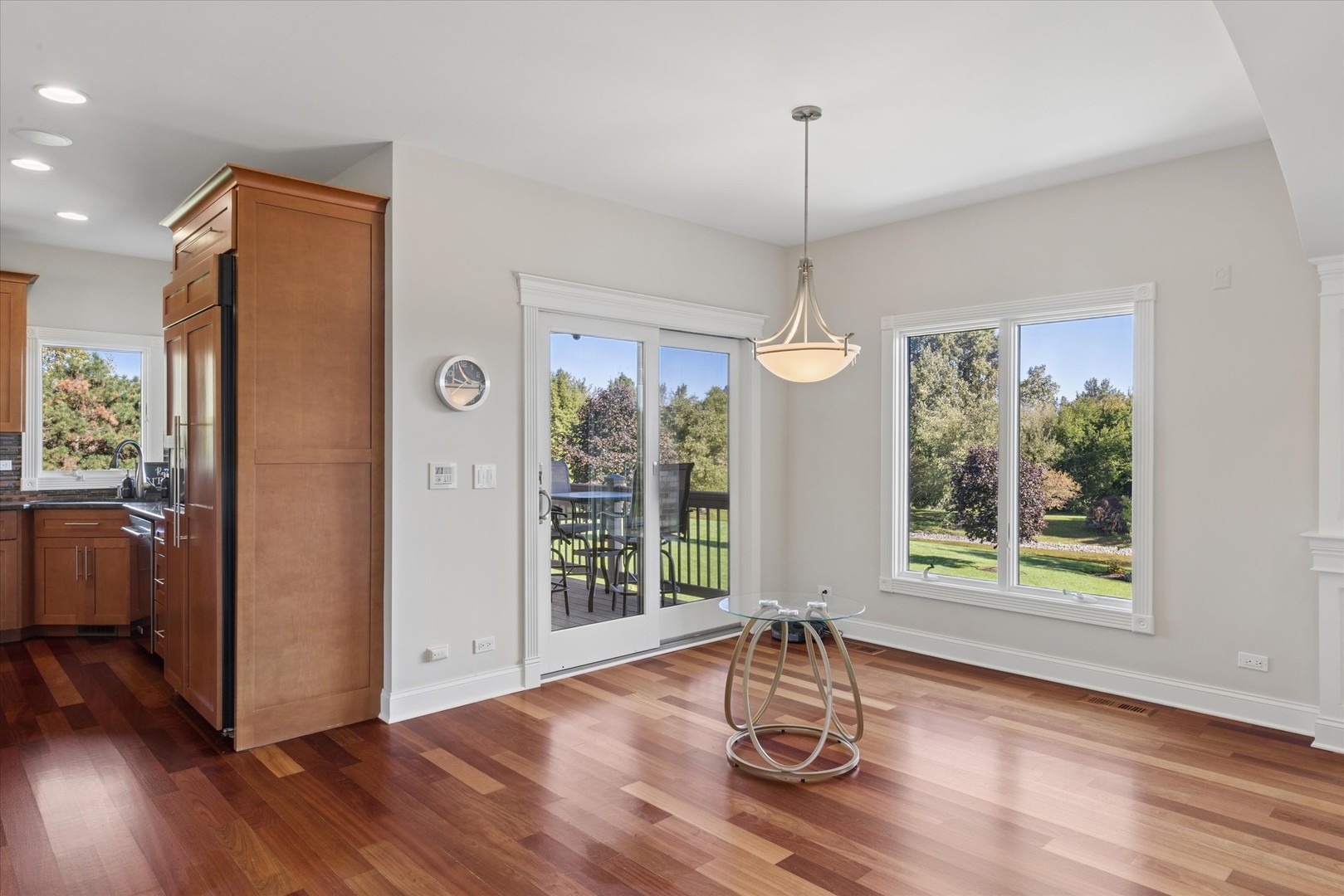 Dining area with hardwood floors, a glass-top table, and windows overlooking the backyard.