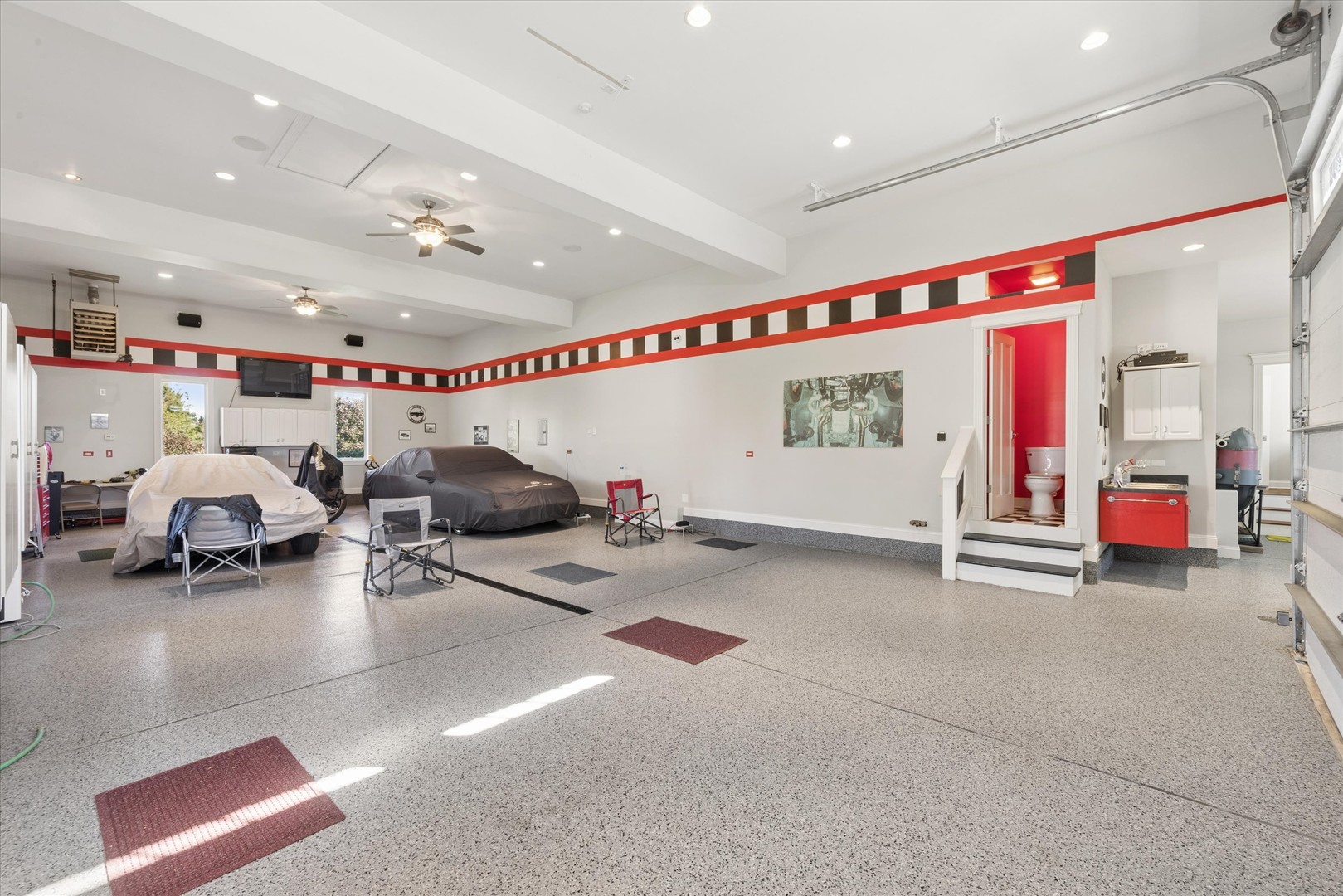 Spacious garage with covered cars, a speckled floor, and a small raised bathroom area.