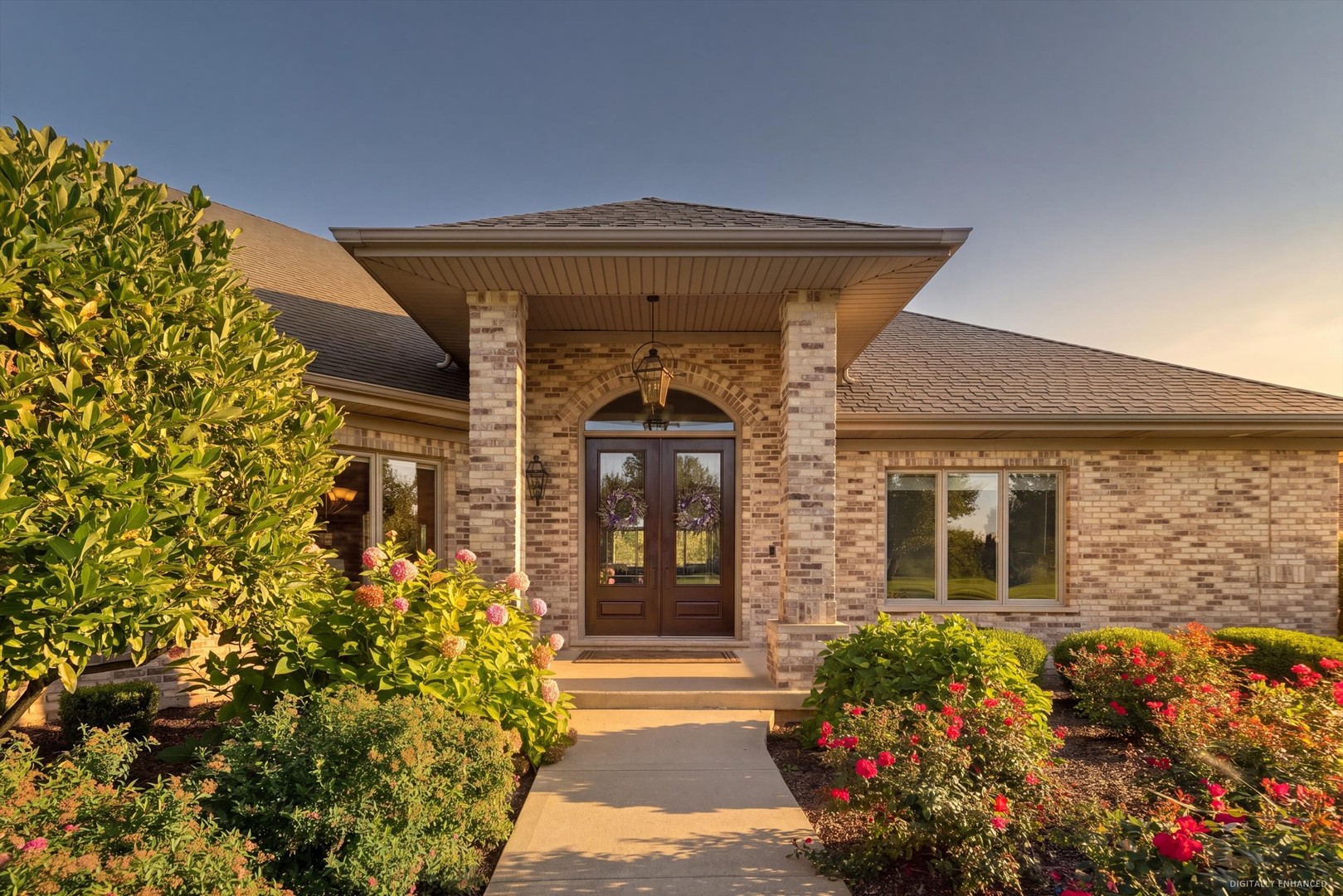 Brick home entrance with a covered porch, double doors, and colorful landscaped gardens.