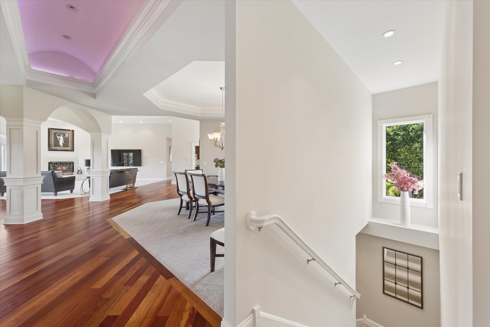Open living and dining area beside a bright staircase, with hardwood floors and a purple-lit tray ceiling.
