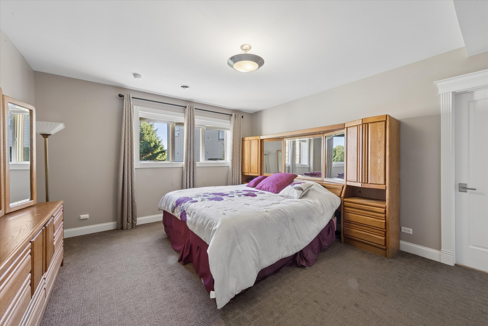 Bedroom with a large bed, purple accents, mirrored wood cabinetry, and curtained windows.
