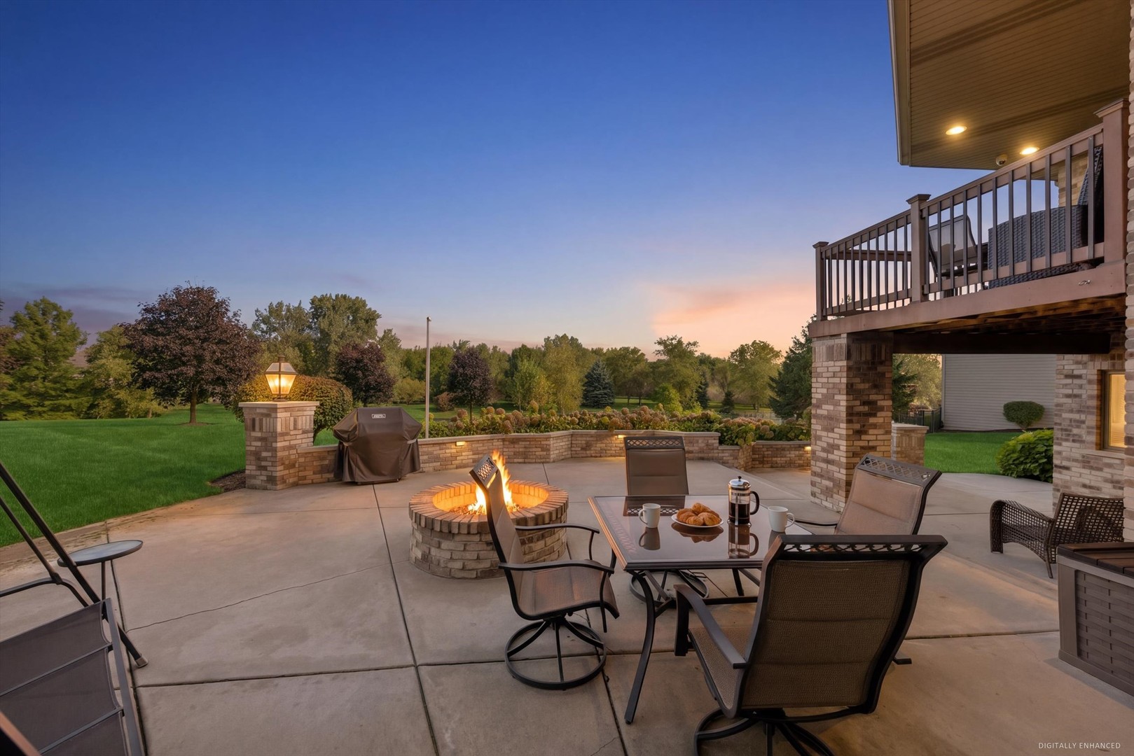 Backyard patio with a glowing fire pit, outdoor dining set, and raised deck at dusk.
