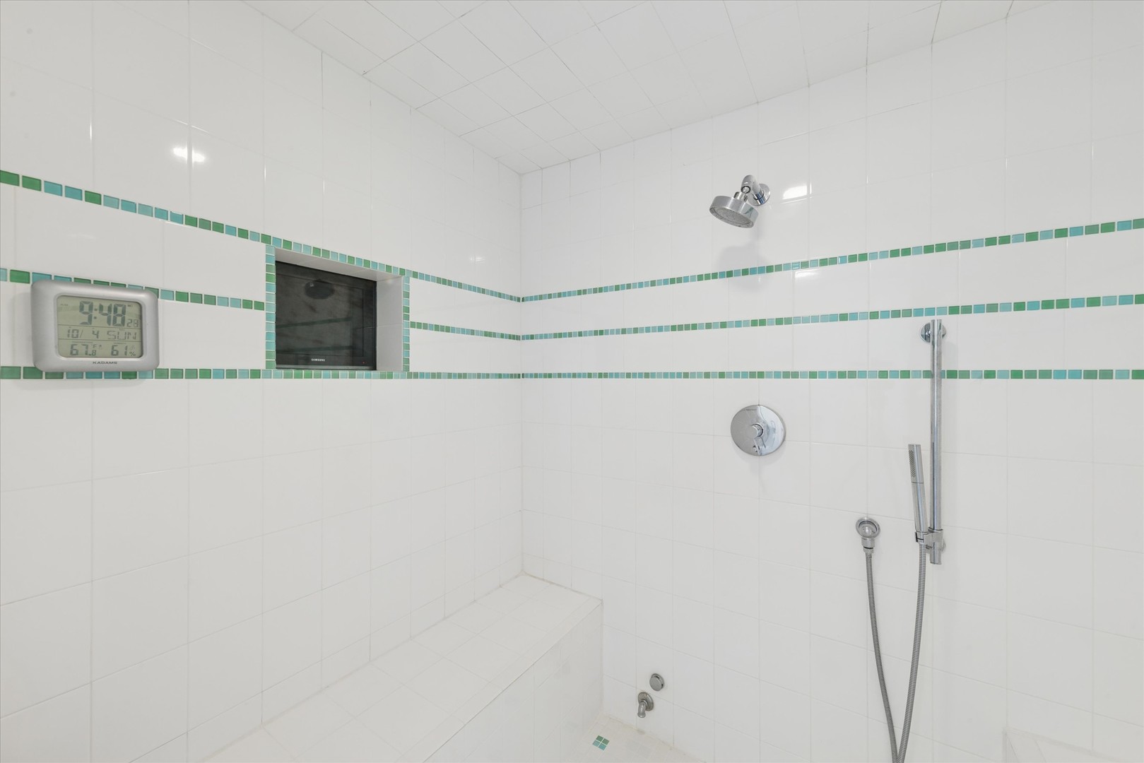 Walk-in shower with a tiled bench, green mosaic stripes, and handheld sprayer.
