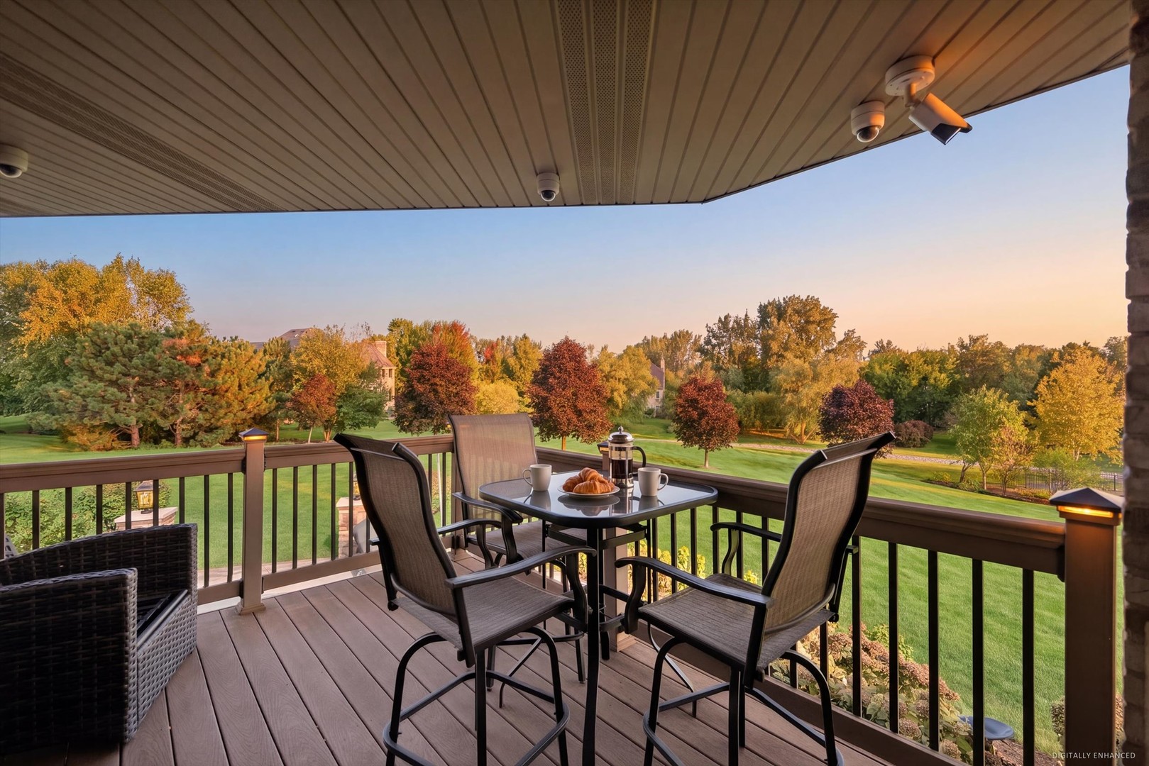 Covered deck with outdoor dining furniture overlooking a lawn and colorful autumn trees.