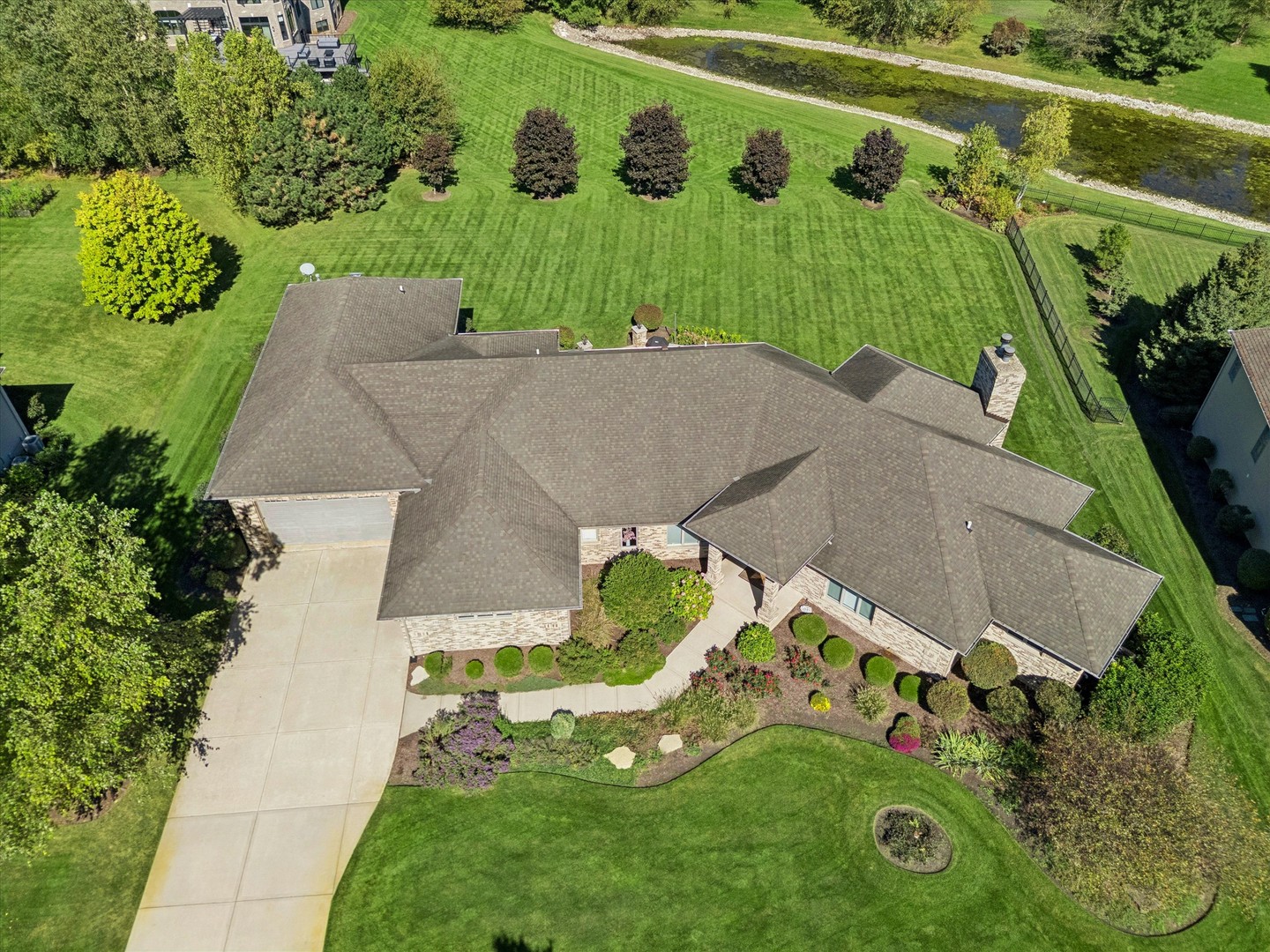 Aerial view of a brick home with a broad manicured lawn and creek behind it.