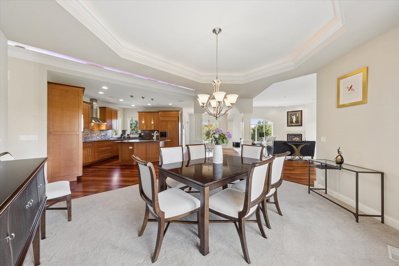 Dining room with a dark wood table and chandelier, opening onto a warm wood kitchen and sitting area.
