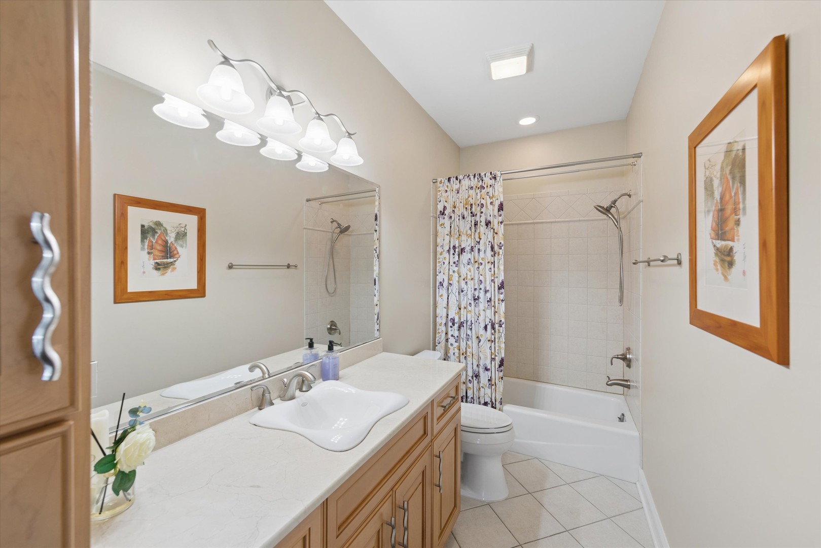 Bathroom with a long wood vanity and tiled tub-shower behind a floral curtain.
