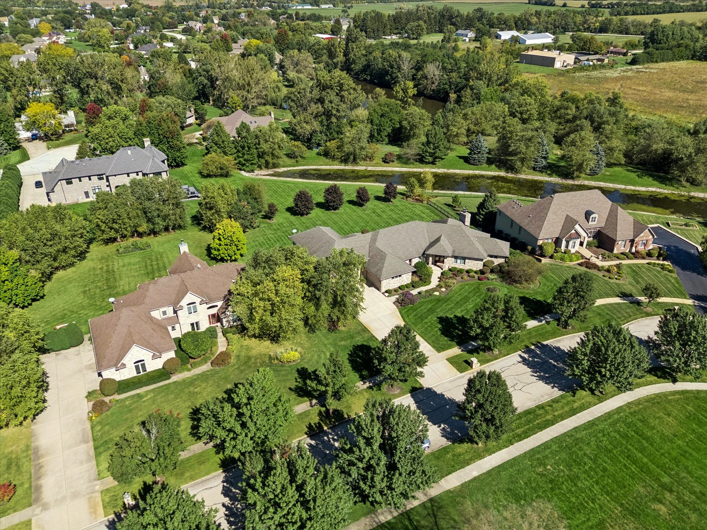 Aerial view of large homes and green lawns beside a landscaped creek.
