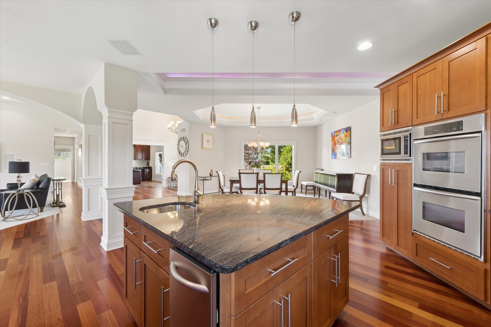Kitchen with a large granite island, cherry cabinetry, stainless steel double ovens, and an adjoining dining area.