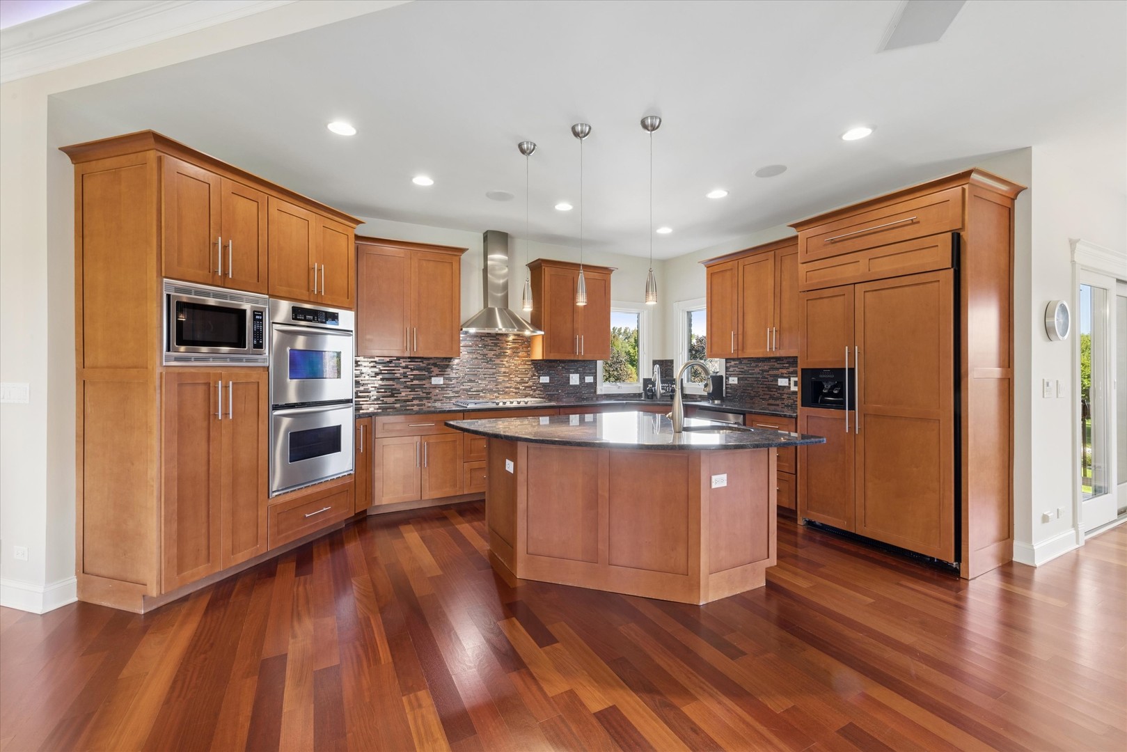 Kitchen with warm wood cabinetry, a large island, stainless steel appliances, and hardwood floors.