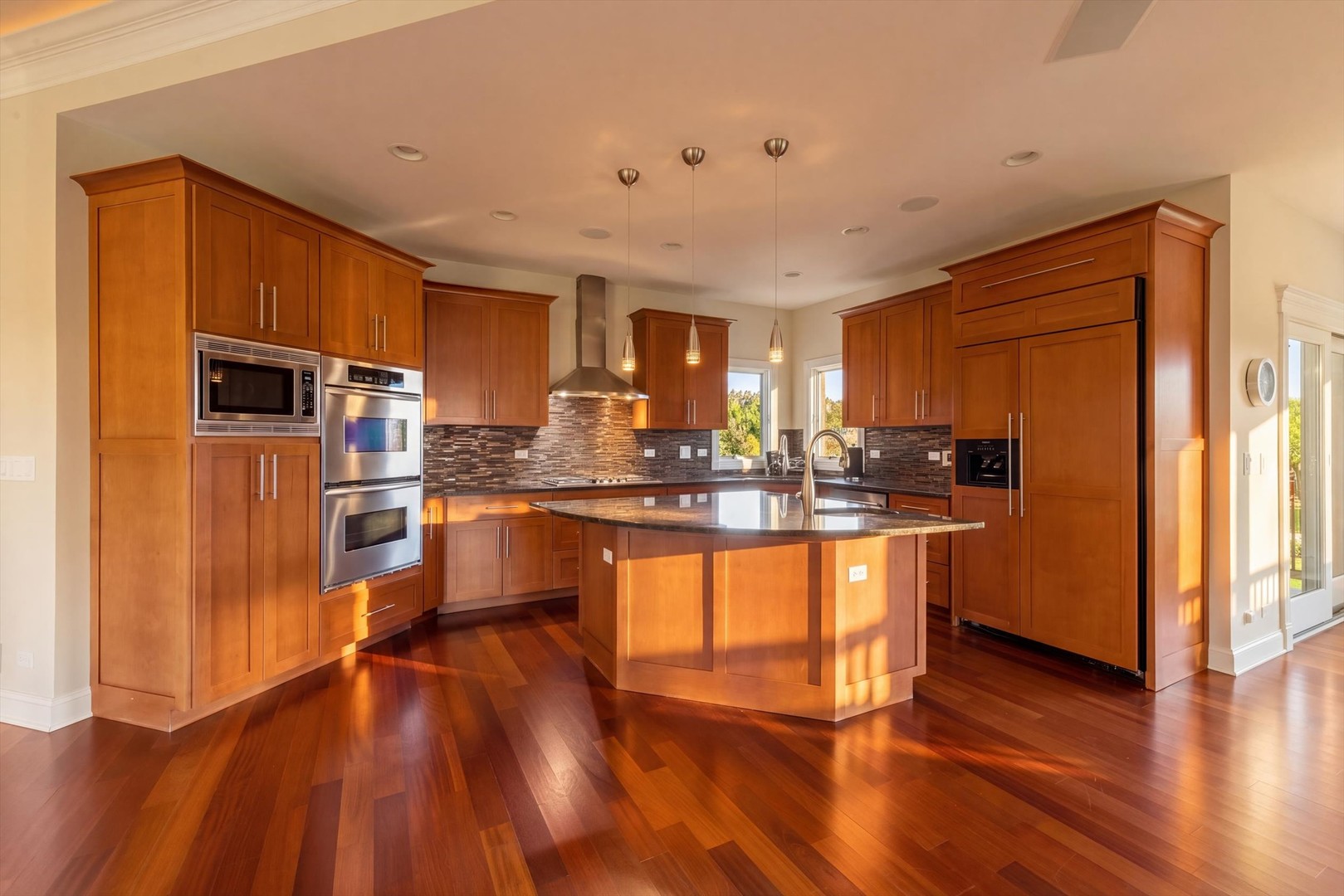 Kitchen with a large island, warm wood cabinets, stainless steel double ovens, and hardwood floors.