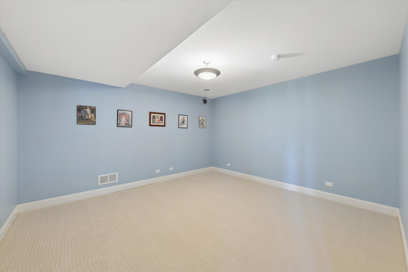 Empty blue-walled room with beige carpet, framed pictures, and a raised tray ceiling.