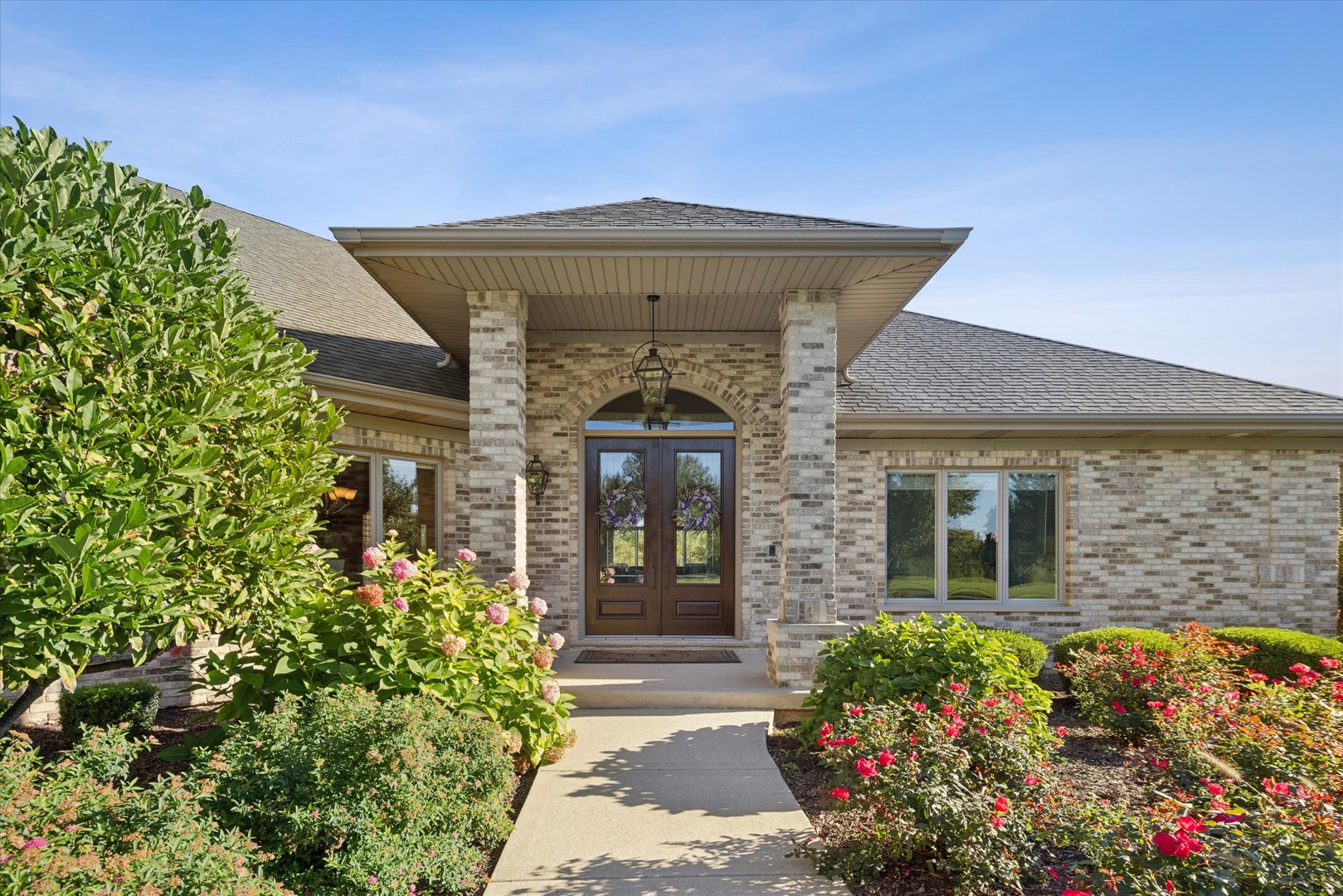 Brick home with a covered entry, dark double doors, and colorful flower gardens.