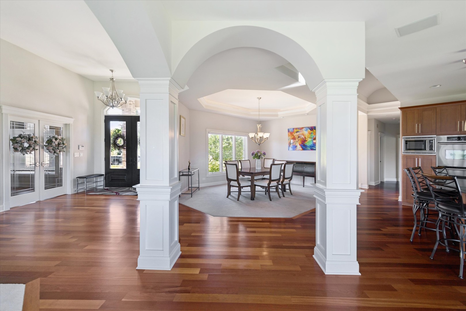 Open dining room with a white arched opening, hardwood floors, and a view into the kitchen.