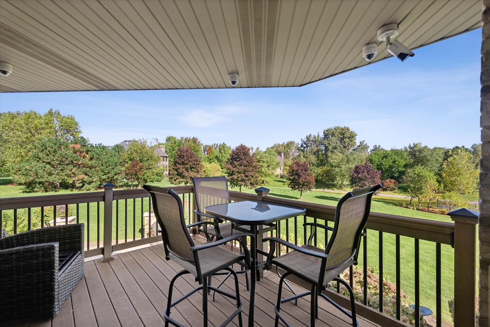 Covered deck with dining set overlooking a landscaped lawn and mature trees.