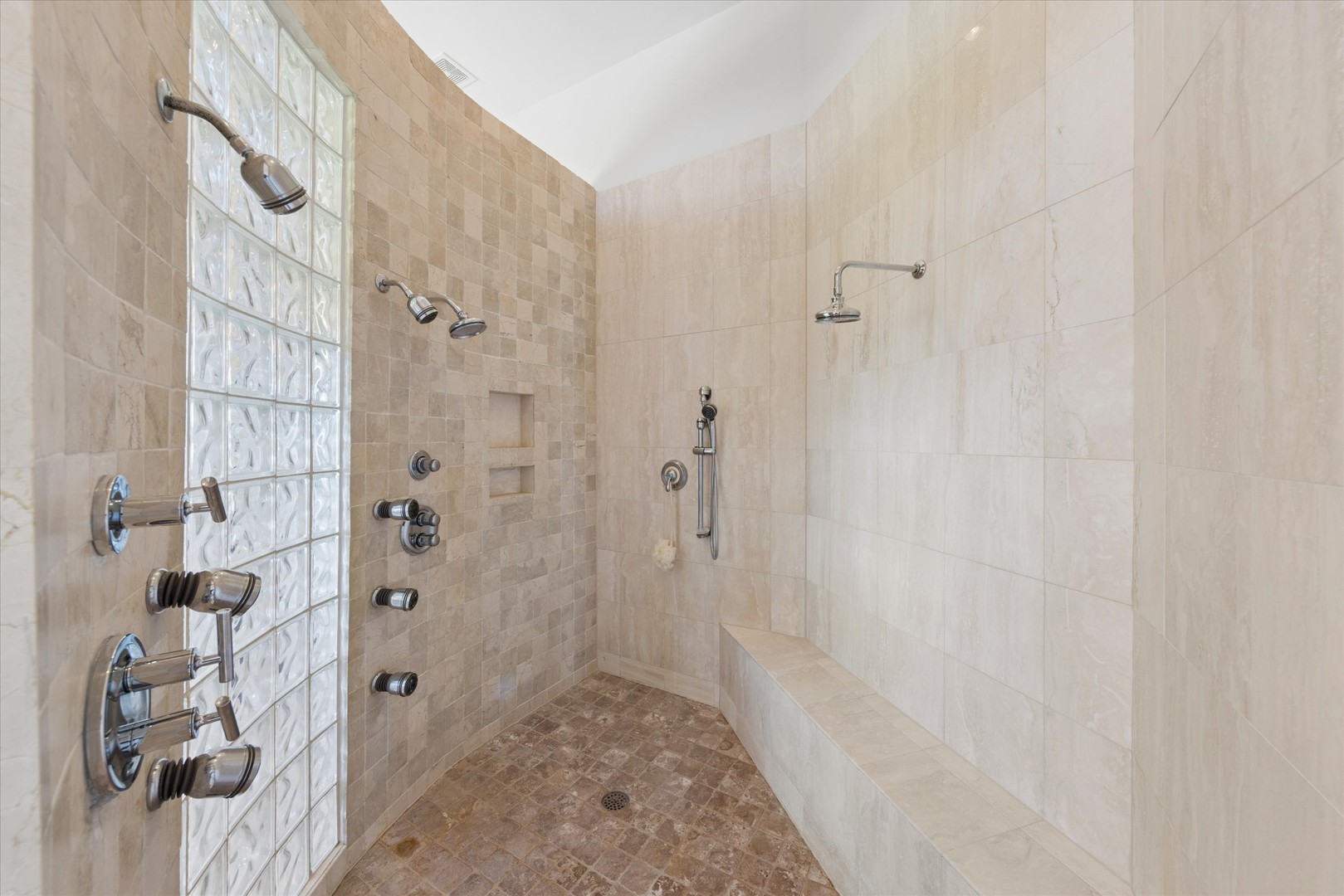 Walk-in shower with multiple showerheads, a glass-block partition, and a built-in tiled bench.