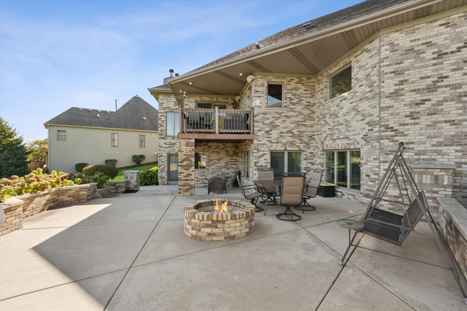 Brick home’s rear patio with a circular fire pit, outdoor seating, and an elevated balcony.