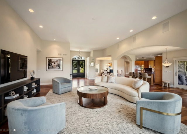 Living room with a curved cream sectional, pale blue armchairs, and round wood coffee table.