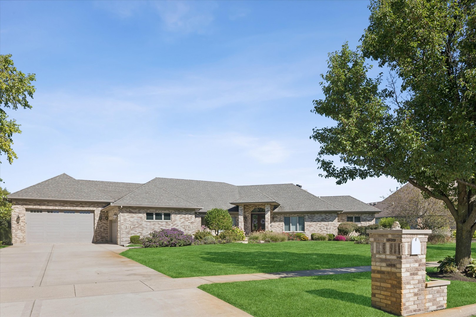 Single-story brick home with an attached two-car garage, landscaped lawn, and brick mailbox pillar.