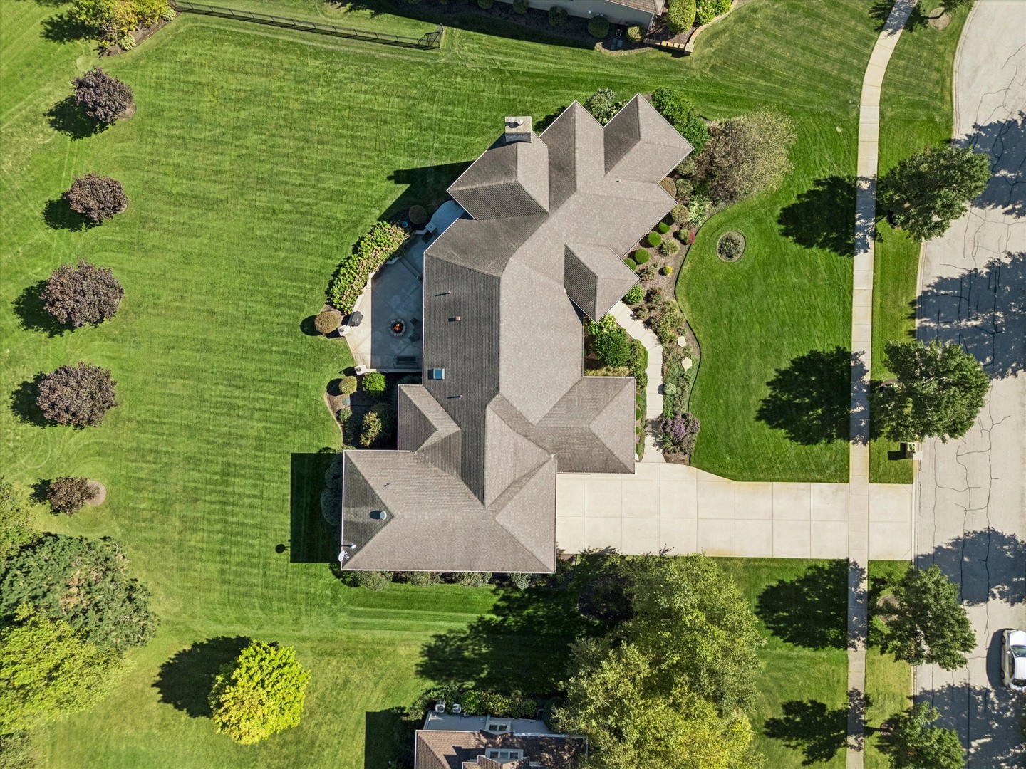 Aerial view of a large home surrounded by landscaped lawn, with a driveway and patio fire pit.