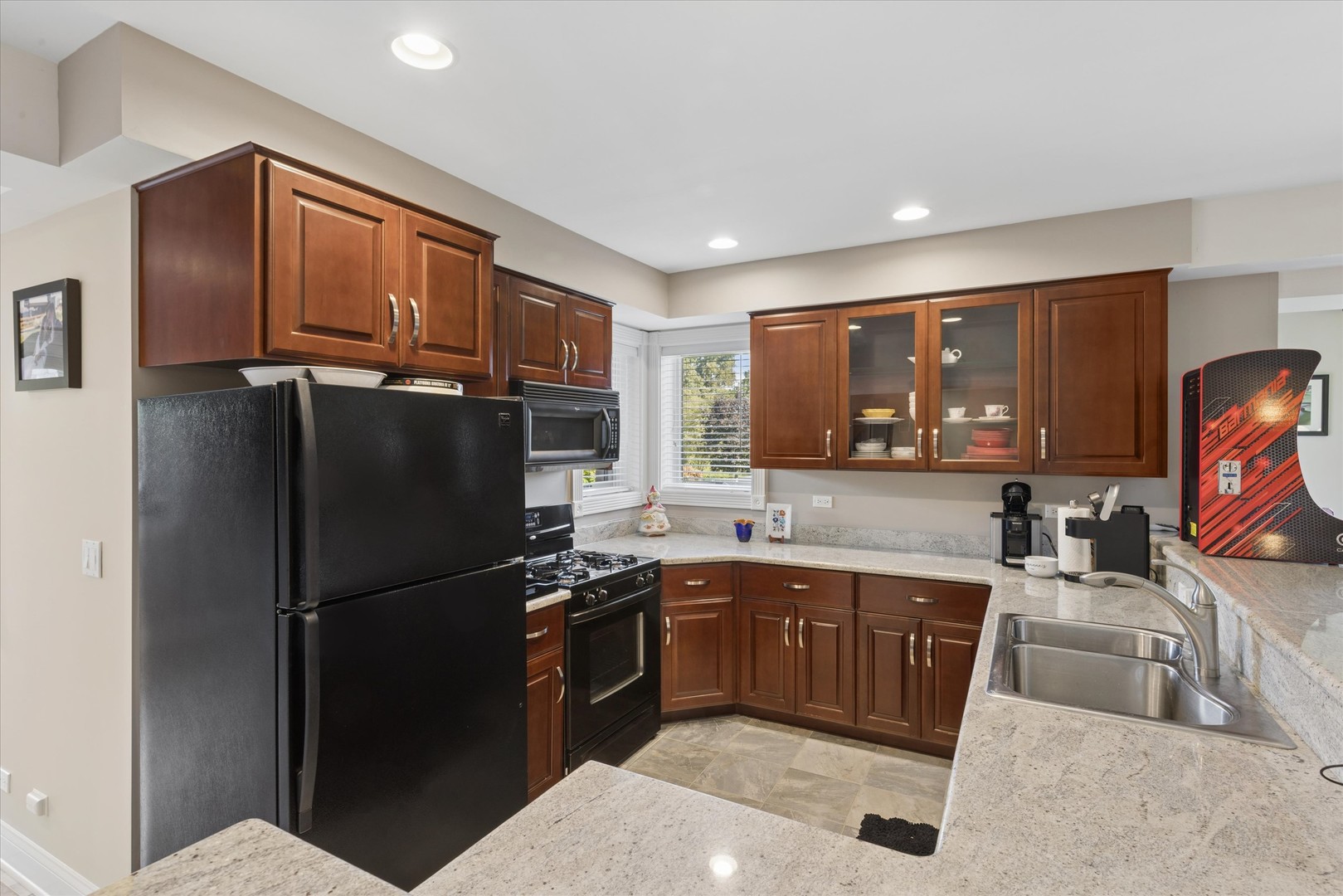 Kitchen with cherry cabinets, granite counters, black appliances, glass-front cupboards, and a double-basin sink.