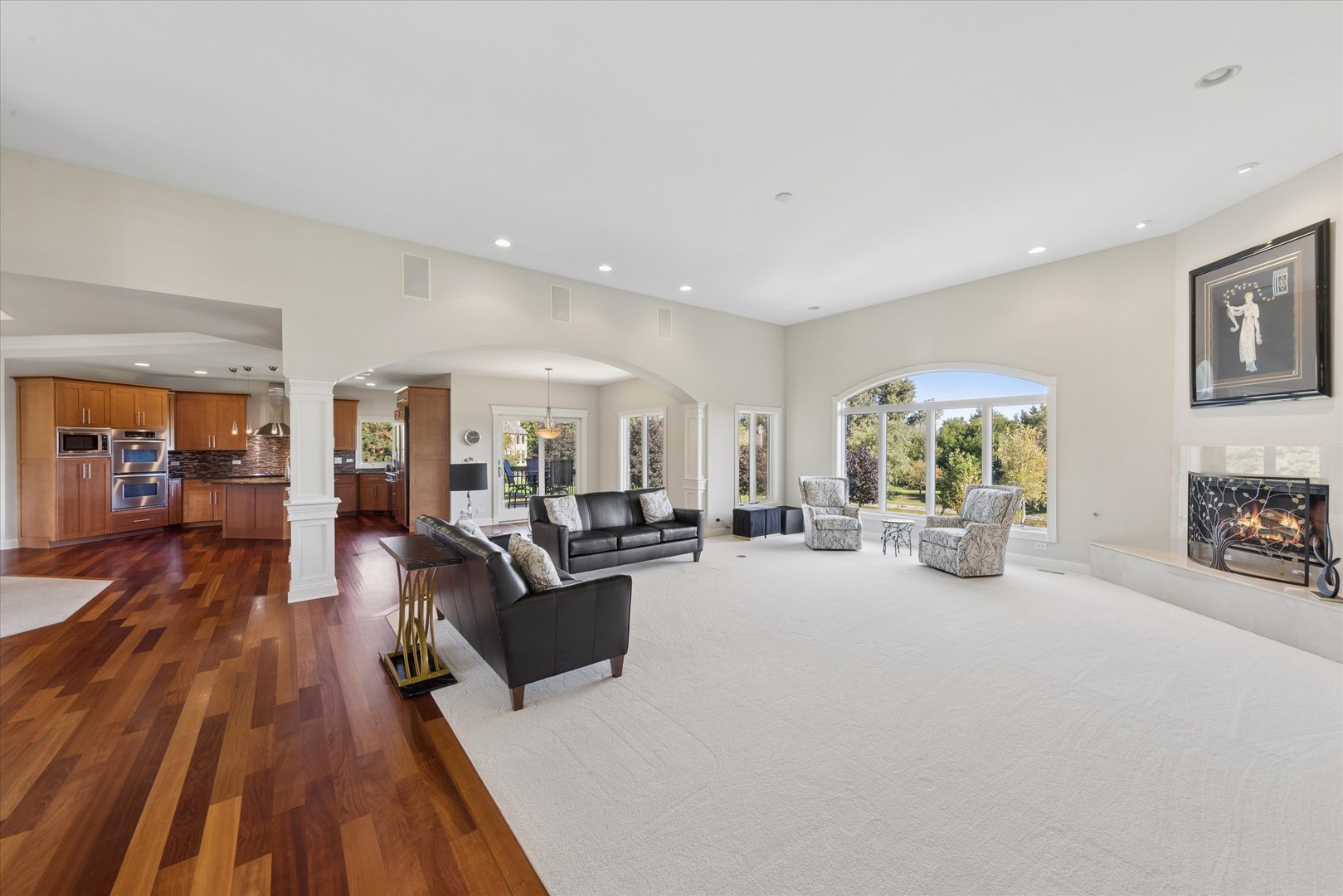Living room with an arched picture window, fireplace, hardwood floors, and open kitchen.