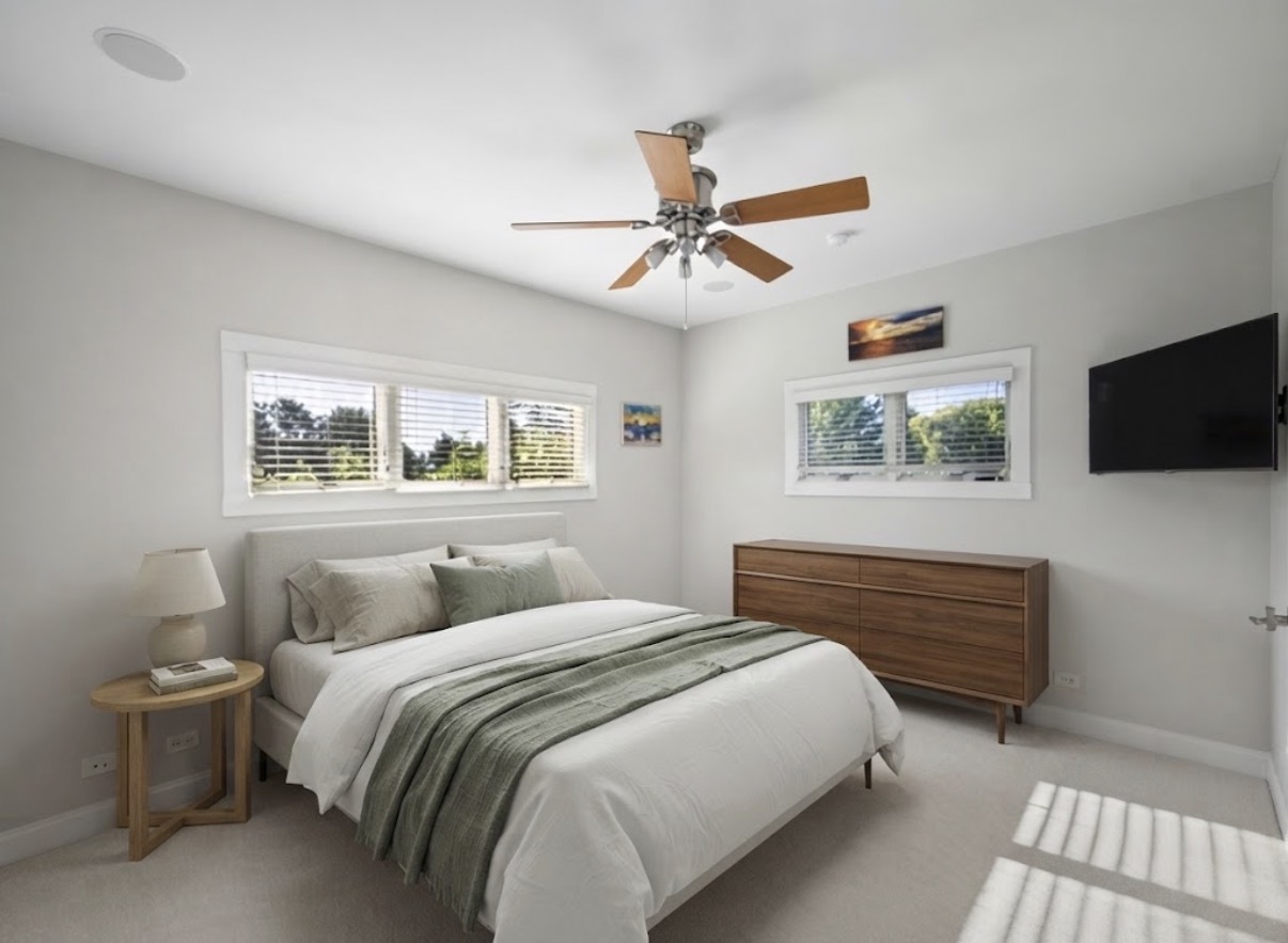 Staged bedroom with white and sage bedding, two windows, a wood dresser, and a ceiling fan.