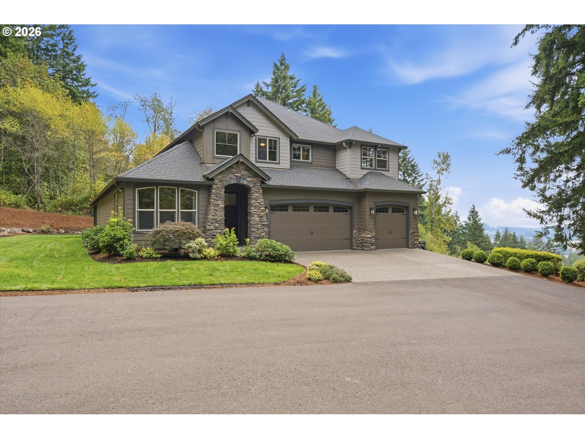 Two-story taupe house with a stone entry, double garage, and landscaped lawn among mature trees.