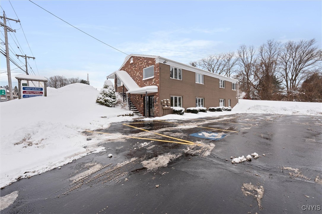Two-story commercial building with brown siding, brick accents, and a snow-covered accessible parking lot.
