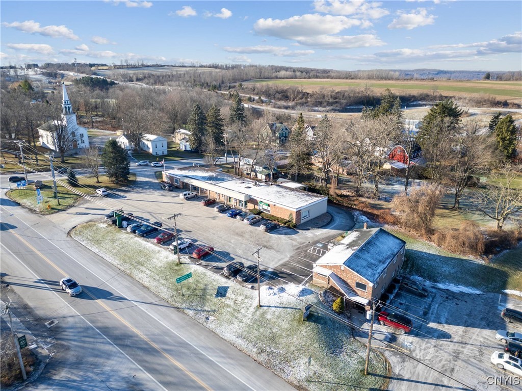 Aerial view of roadside commercial buildings and parking beside a two-lane road, with light snow and open fields beyond.