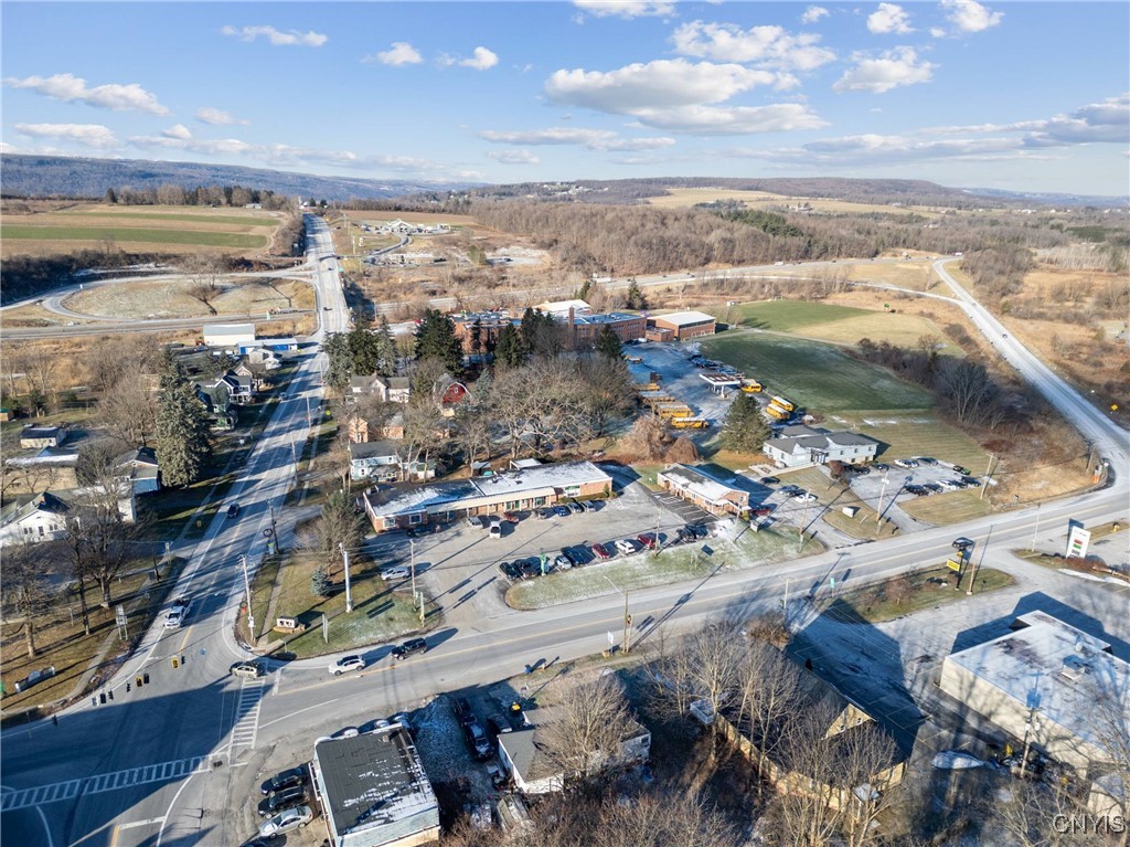 Commercial buildings and school buses beside a rural highway intersection, viewed from above.