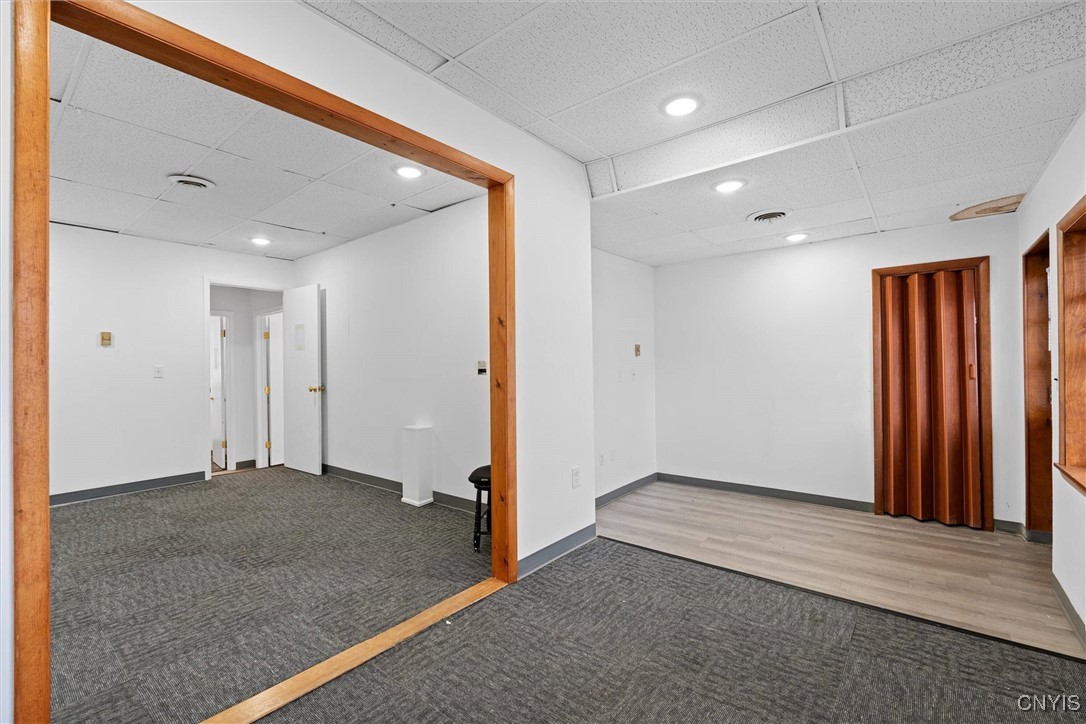 Vacant interior room with gray carpet, light wood-look flooring, and a wood-framed opening.