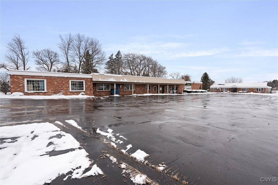 Single-story brick commercial building behind a wet parking lot, with snow along the edges.
