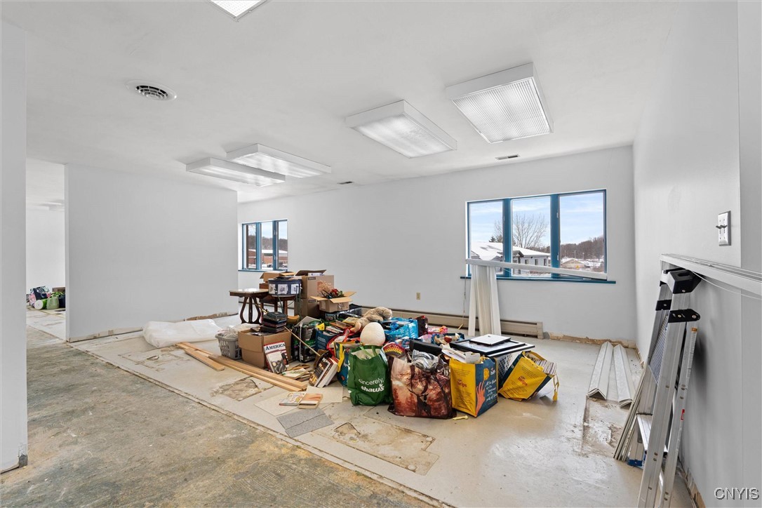 Unfinished room with fluorescent lights, large windows, and construction materials and supplies piled on the floor.