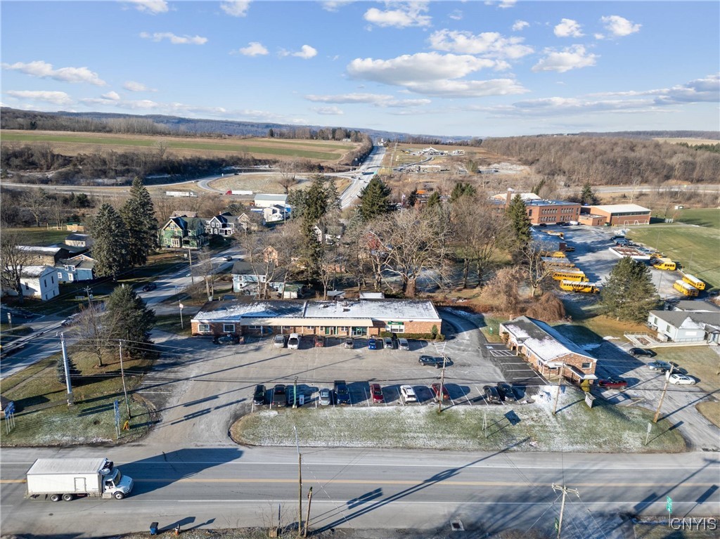 Aerial view of a brick commercial building and parking lot beside Route 11, with fields and a bus lot nearby.