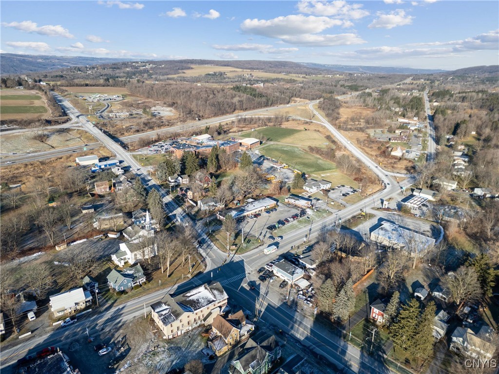 Aerial view of Route 11 and surrounding buildings, with open fields and wooded hills beyond.
