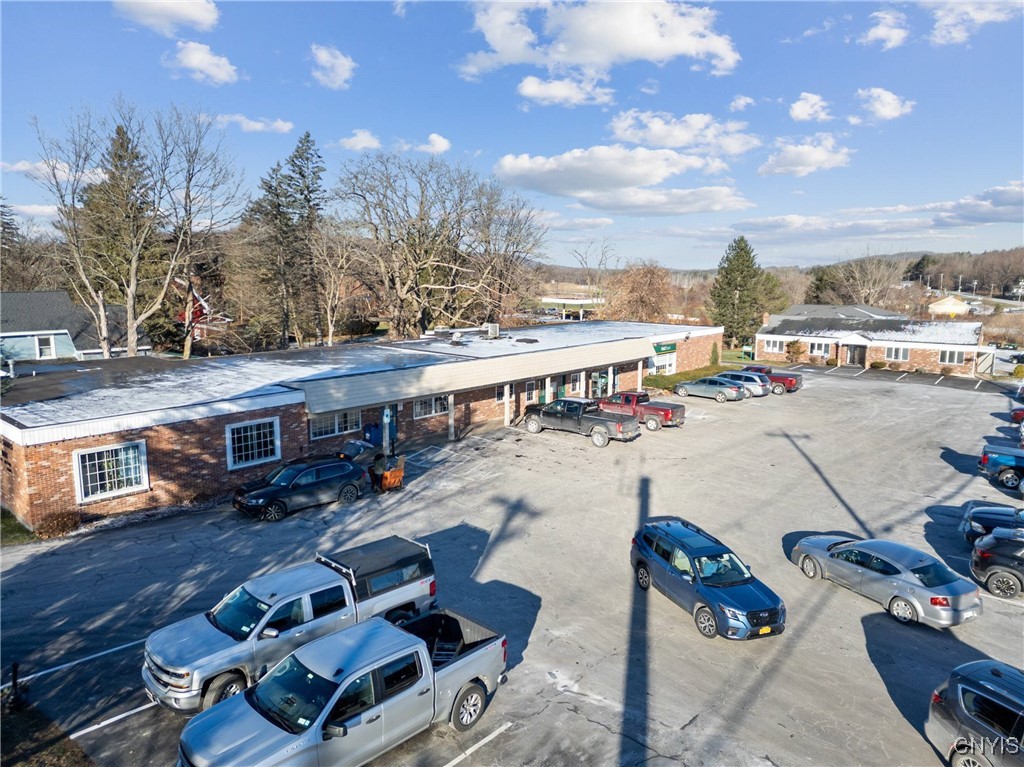 Aerial view of a brick commercial building and parking lot with numerous parked vehicles.