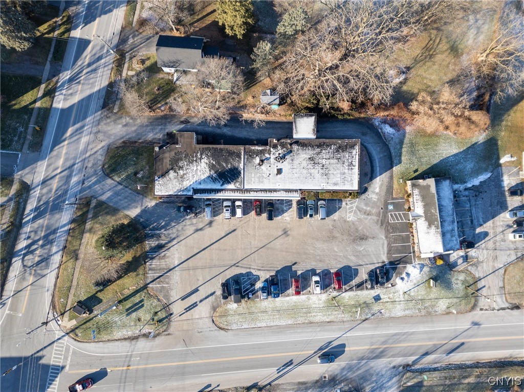 Aerial view of a commercial building and parking lot at a road intersection, with cars and patches of snow.