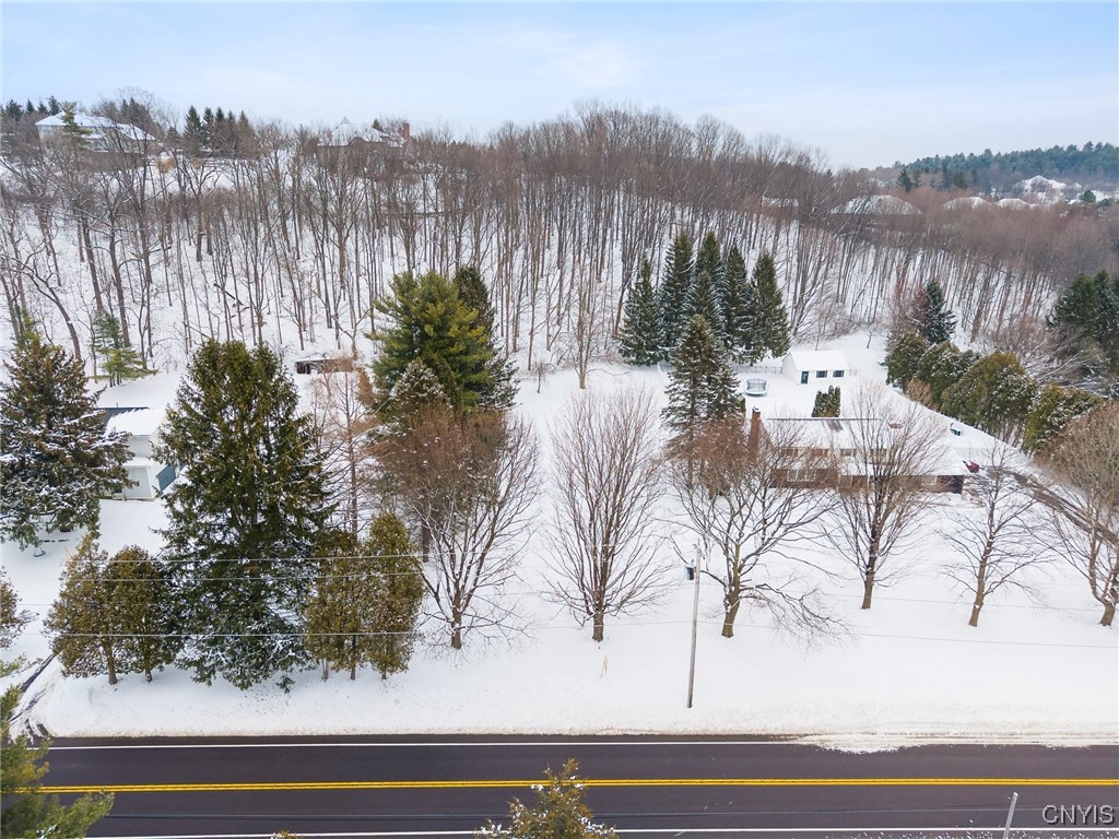 Snow-covered property beside a two-lane road, surrounded by trees and woodland.
