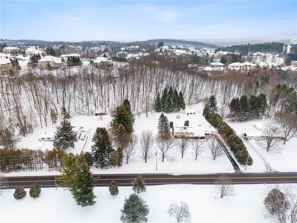 Aerial view of a snow-covered home and wooded lot beside a two-lane road.